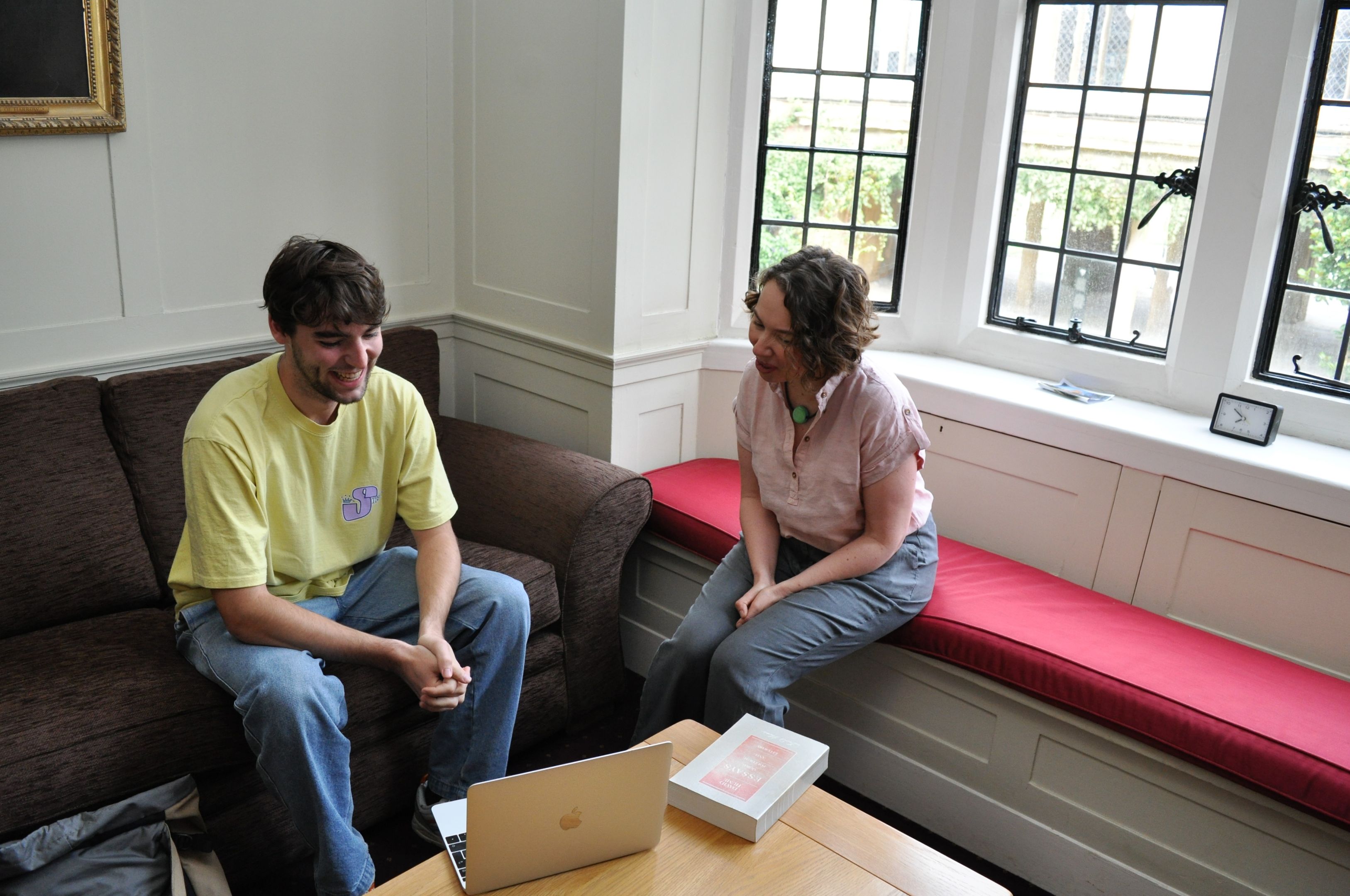 A young man and a woman sitting in a room with bay windows engaged in a supervision. 