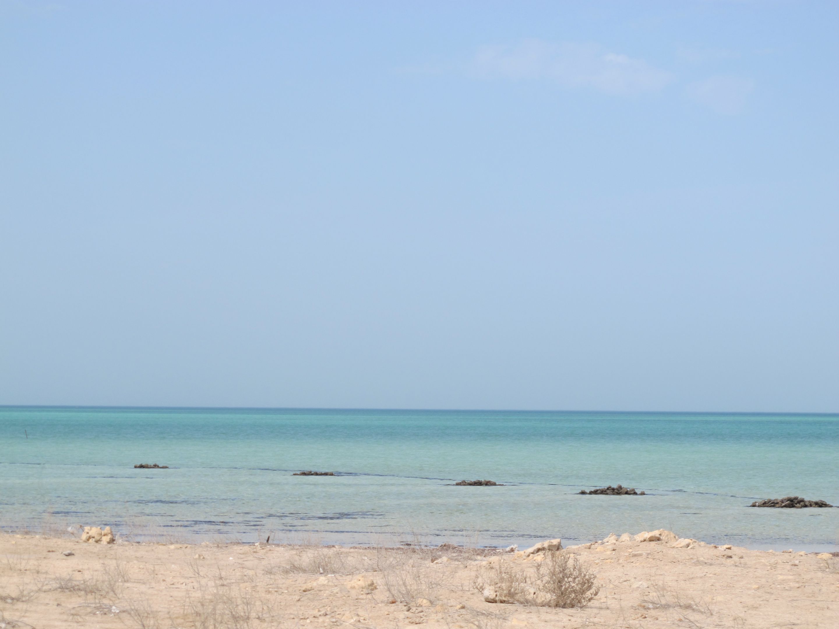 View across a rocky and sandy scene towards turquoise blue sea and sky