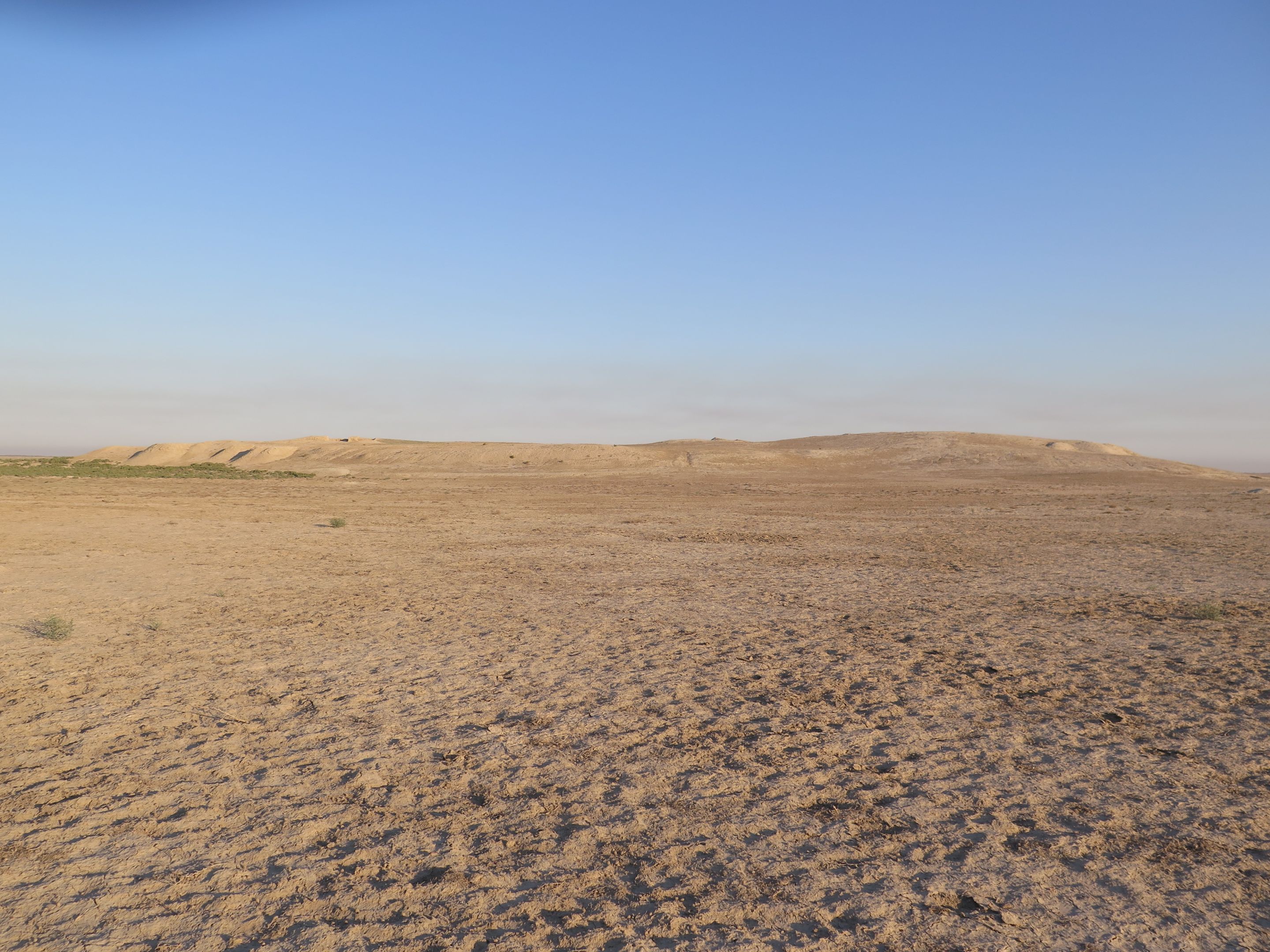 Arid desert landscape with archaeological mound in the distance, blue sky above