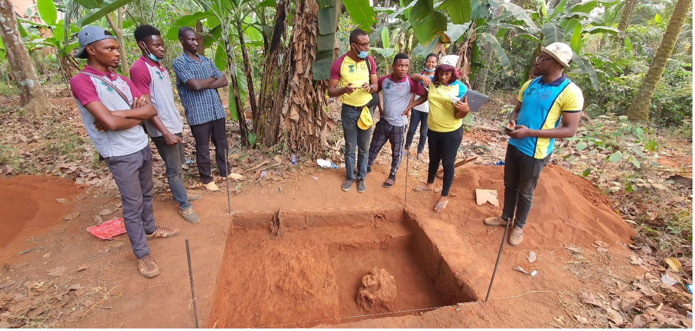 Eight people standing around an archaeological excavation in a forrest.