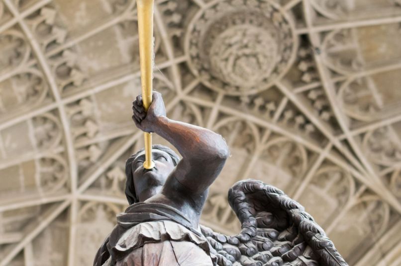 Wooden angel sculpture with trumpet below a carved ceiling