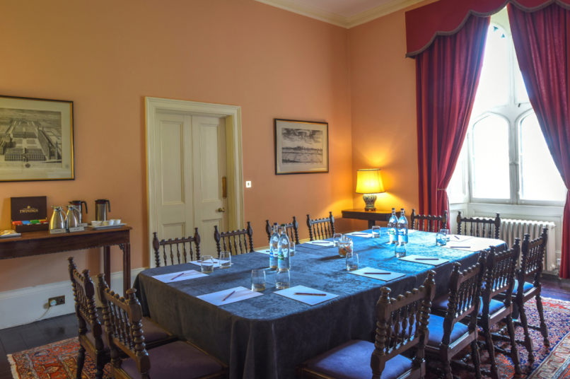 A room with a meeting table and chairs, with red curtains and a tall window to the right