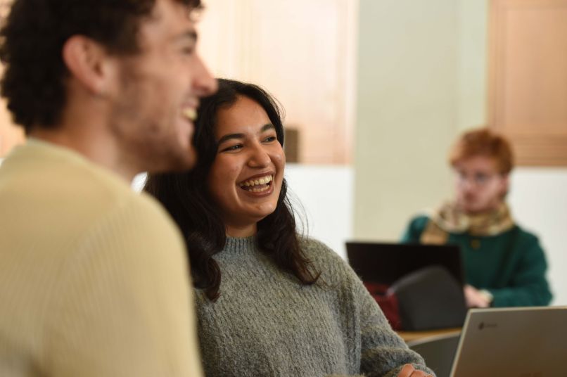 Two students smiling in the bar in front of a laptop.