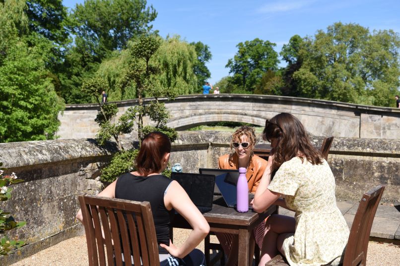 Two students and a supervisor in Bodley's court working on a table in the sun