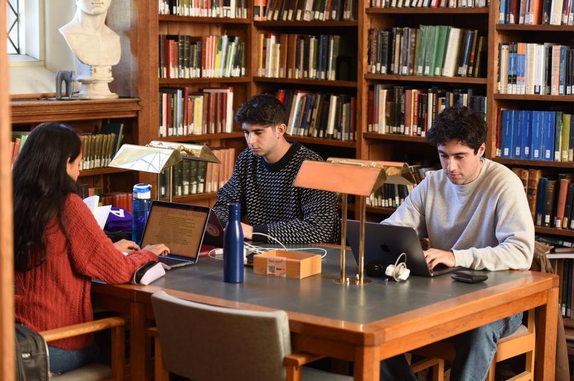three students sit around a table in the library working