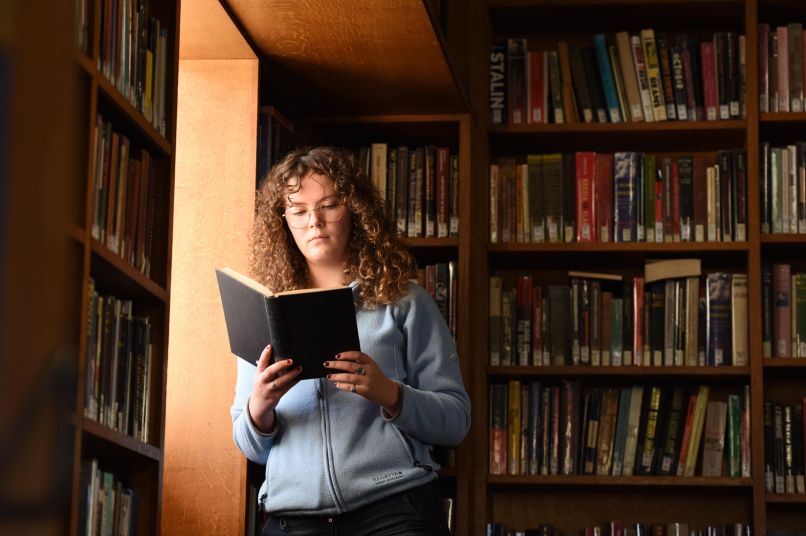 A student standing in the library reading a book