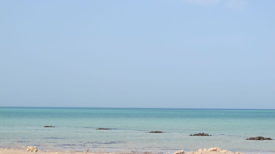 View across a rocky and sandy scene towards turquoise blue sea and sky