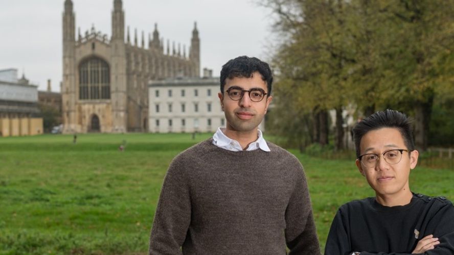 Two smiling men wearing glasses stand in front of King's College Chapel and the Gibbs building