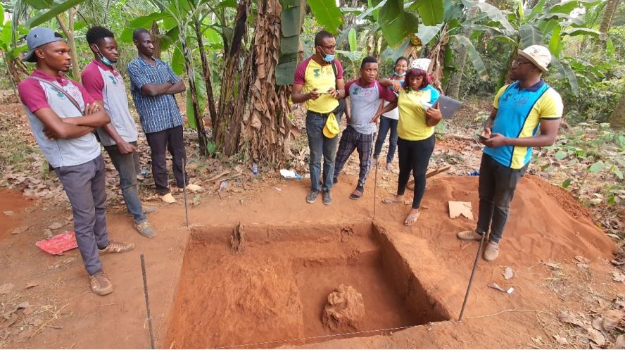 Eight people standing around an archaeological excavation in a forrest.