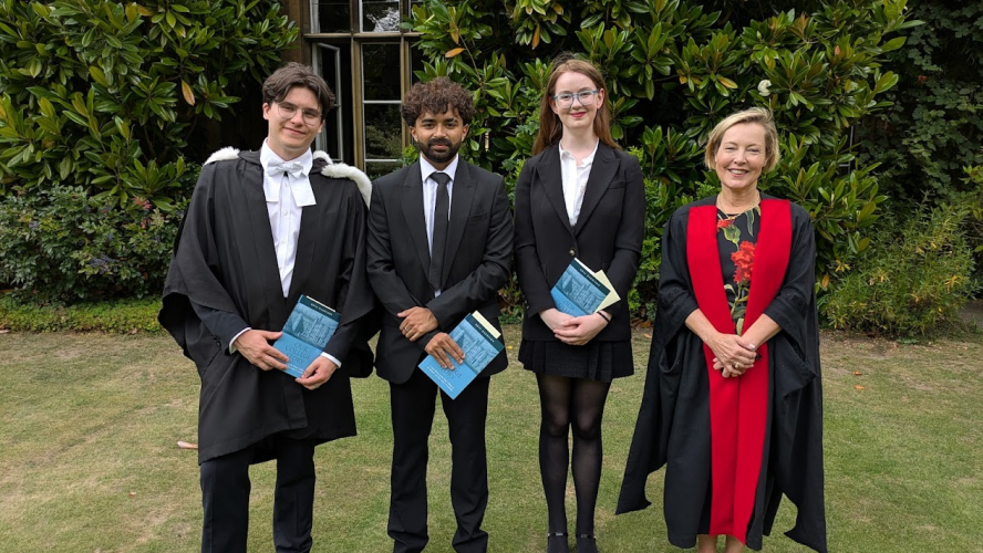 Three students holding books with the Provost, all wearing academic dress in a garden
