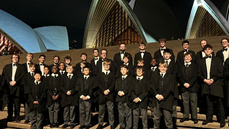 A smiling group of men and boys wearing black tie stand outside the Sydney Opera House at night
