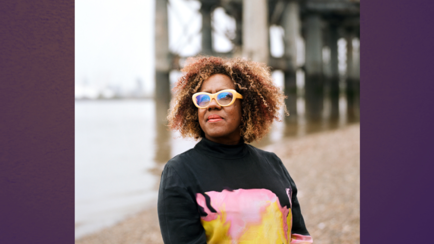 A woman curly hair and yellow glasses stands beside a pier 
