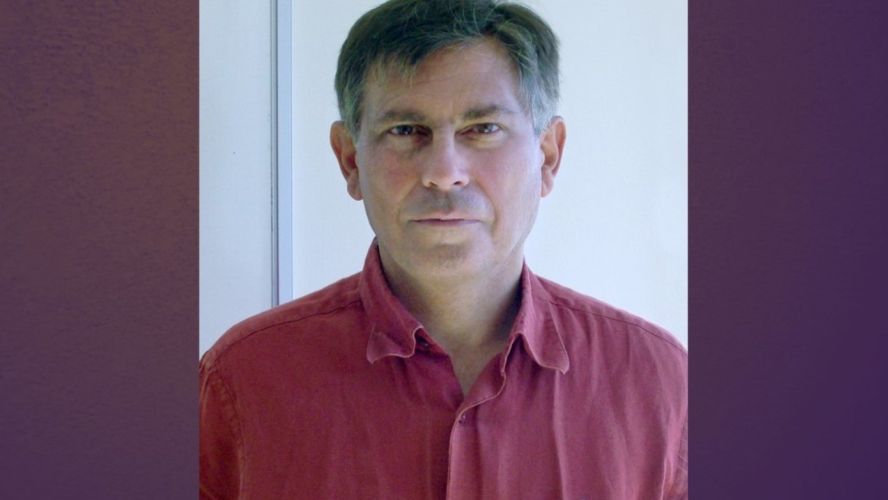 A smiling man with dark grey hair and a red shirt