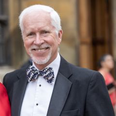 a man with white hair and a bow tie smiles at the camera