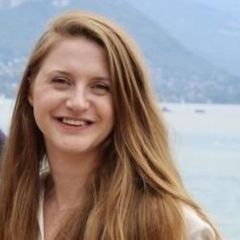 A smiling woman with long blond hair with a lake and mountain in the background