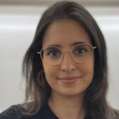 A smiling woman with long brown hair wearing glasses with a white background.