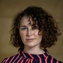 A white woman with curly dark hair wearing a striped top