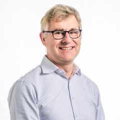 A smiling man with glasses wearing a pale shirt