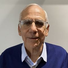 Man with glasses and a blue jumper over a pale blue shirt