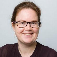 A smiling lady with glasses wearing a dark shirt