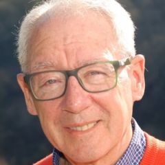 Gentleman with short grey hair and glasses, wearing a red jumper over a blue shirt