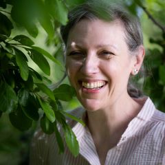 A smiling women wearing a shirt surrounded by greenery