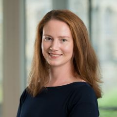 a smiling woman with ginger hair, wearing a dark blue top. 