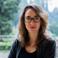 A woman with glasses and shoulder long dark blond hair in front of trees.