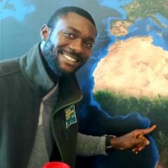 A smiling man with short dark hair and beard pointing at a map. 