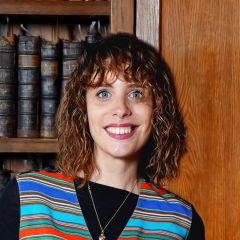 Giulia Boitani, a smiling woman with curly brown hair wearing a stripey waistcoat standing in front of some old books on a shelf