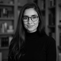 Georgia Nasseh, a black and white image of a smiling woman with long dark hair and glasses wearing a dark jumper