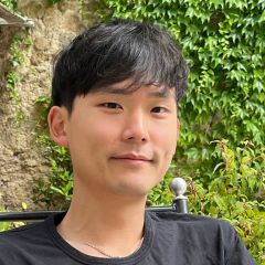 A smiling man with dark hair and wearing a dark shirt in front of an ivy covered wall. 