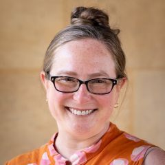 Janet Davis, smiling woman wearing glasses and an orange and pink spotted top.