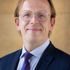 Marcus Boeick, a smiling man with short blonde hair, glasses and a navy suit jacket, light blue shirt and blue tie. 