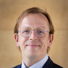 Marcus Boeick, a smiling man with short blonde hair, glasses and a navy suit jacket, light blue shirt and blue tie. 