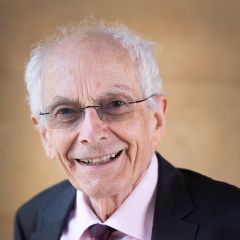 Martin Hyland, a smiling man with short grey hair and glasses. He is wearing a pink shirt and a black jacket.
