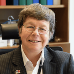 A woman with short brown hair and glasses with books behind her smiles at the camera