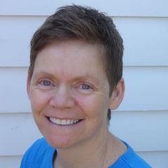 a smiling woman with very short hair wearing a light blue top. 
