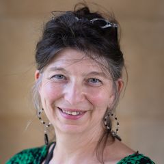 Rosanna Omitowoju, a smiling woman with brown hair tied back and read reading glasses on her head. She is wearing a green and black patterned top. 