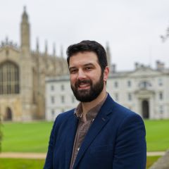 A smiling man with dark beard, wearing a blue blazer, with the Gibbs building and King's College Chapel in the background