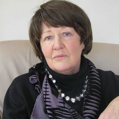 Aileen Kelly, a woman with short dark hair wearing a black top, geometric scarf and silver necklace. 