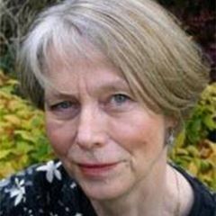 Anne Cooke, a smiling woman with short grey hair and blue eyes. She is in a leafy outdoor space