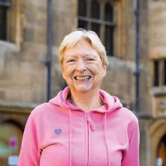 A smiling woman with short blond hair wearing a pink jumper