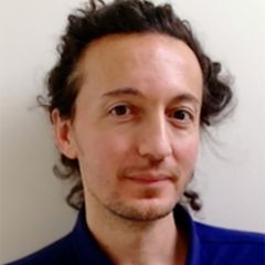 Aytek Erdil, a smiling man with long brown curly tied back hair and a dark blue shirt