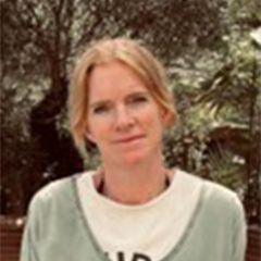 A smiling woman with blonde hair standing in a leafy place