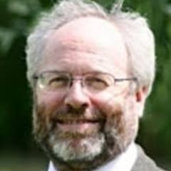 David Munday, a smiling man with grey hair, a beard and glasses and wearing a suit. He is standing outdoors in a green space.
