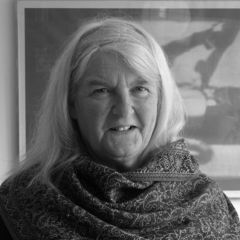 A black and white image of a smiling woman with white hair wearing a scarf around her neck.