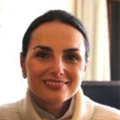 Elisa Faraglia, a smiling woman with dark hair tied back. She is wearing a cream jumper.
