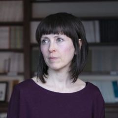 Ferdia Stone Davis, a woman with short black hair wearing a purple top. She is standing in a study