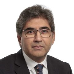 Fraz Mir, a smiling man with dark hair and glasses wearing a suit and tie